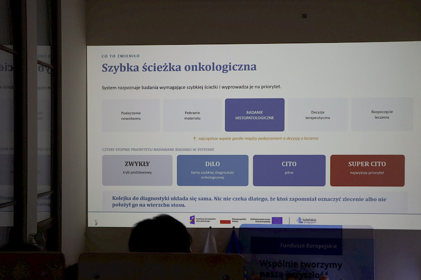 Pod sufitem na dużym ekranie wyświetlona jest informacja co zmieniło się w szpitalu po wprowadzeniu systemu cyfryzacji.