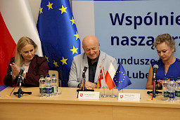 Marszałek Województwa Lubelskiego Jarosław Stawiarski uśmiecha się przy mikrofonie. Koło niego siedzi Dyrektor Anna Brzyska oraz Dyrektor Departamentu Zdrowia Małgorzata Skrok.