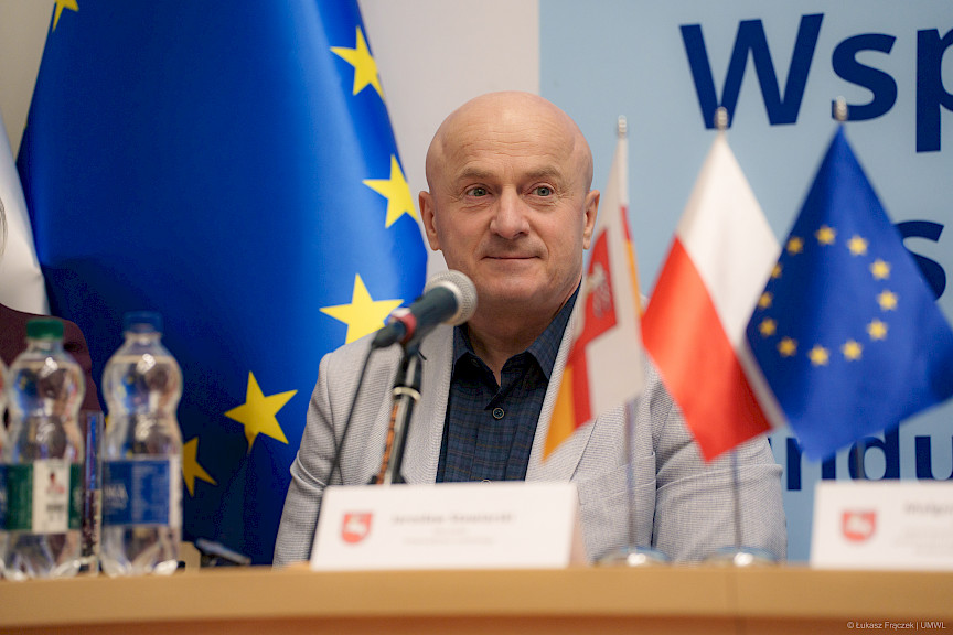 Marszałek Województwa Lubelskiego Jarosław Stawiarski patrzy na wprost siedząc za stołem. Ujęcie twarzy z bliska.