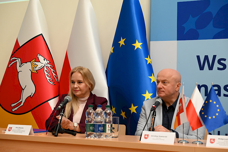 Marszałek Jarosław Stawiarski oraz Dyrektor Anna Brzyska siedzą za stołem i patrzą na kogoś w dal.