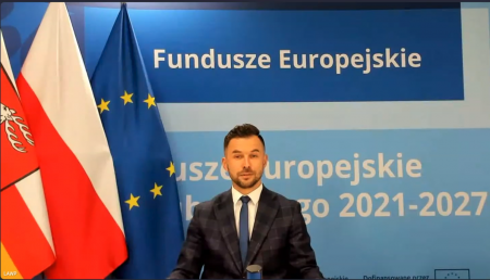 Mężczyzna siedzi przy stole, w tle flagi unie Europejskie, Polski i Województwa Lubelskiego.