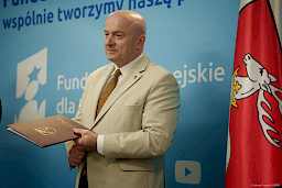Marszałek Województwa Lubelskiego Jarosław Stawiarski stoi i oczekuje na podejście beneficjenta. W rękach trzyma bordową teczkę z umową.