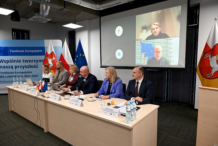 Wicemarszałek Województwa Lubelskiego Piotr Breś wraz z Dyrekcją Departamentu Zarządzania Programami siedzą przy długim stole. Wicemarszałek wypowiada się do mikrofonu prowadząc spotkanie.