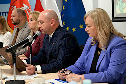 Wicemarszałek Województwa Lubelskiego Piotr Breś wraz z Dyrekcją Departamentu Zarządzania Programami siedzą przy długim stole. Wicemarszałek wypowiada się do mikrofonu prowadząc spotkanie. Ujęcie z bliska.