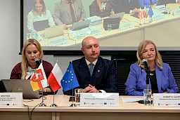  Dyrektor Departamentu Zarządzania Programami Regionalnymi Anna Brzyska wypowiada się do mikrofonu do uczestników posiedzenia. Obok siedzi Wicemarszałek Breś oraz przedstawicielka Komisji Europejskiej.