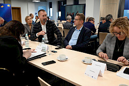 Duża liczba osób siedzących na sali przy stołach podczas posiedzenia Komitetu Monitorującego. Jeden z mężczyzn wypowiada się do mikrofonu z sali. 