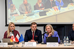 Przedstawicielka Komisji Europejskiej Elżbieta Gajeska wypowiada się do mikrofonu do uczestników spotkania. Koło niej siedzi Dyrektor Departamentu Wdrażania EFS Łukasz Budyńczuk oraz Dyrektor Anna Brzyska.