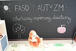 Czarna ściana w jednej z sal terapeutycznych, na której widnieje kredowy napis FASD i Autyzm słuchamy, wspieramy, działamy.