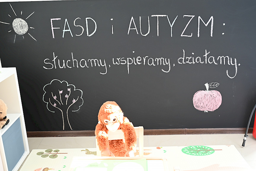 Czarna ściana w jednej z sal terapeutycznych, na której widnieje kredowy napis FASD i Autyzm słuchamy, wspieramy, działamy.