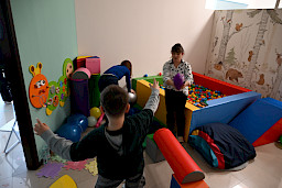 Sala terapeutyczna z basenem z kolorowymi kulkami, w której są dwie kobiety i chłopiec.